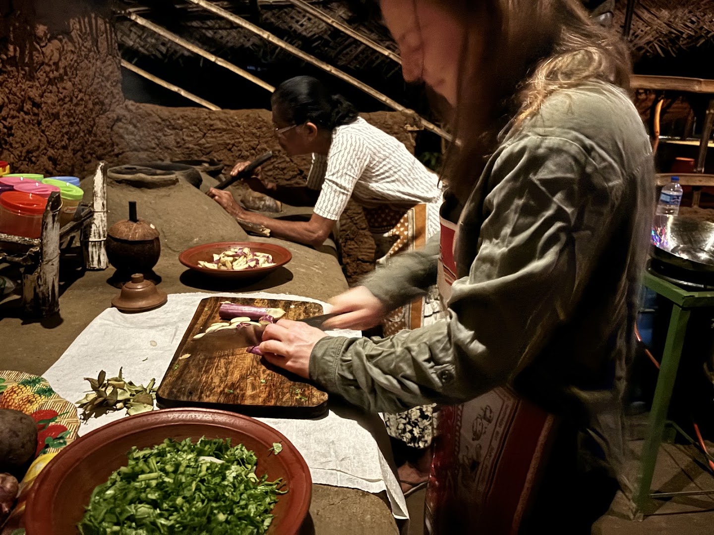 A visitor chopping vegetables beside a cook at a traditional kitchen counter