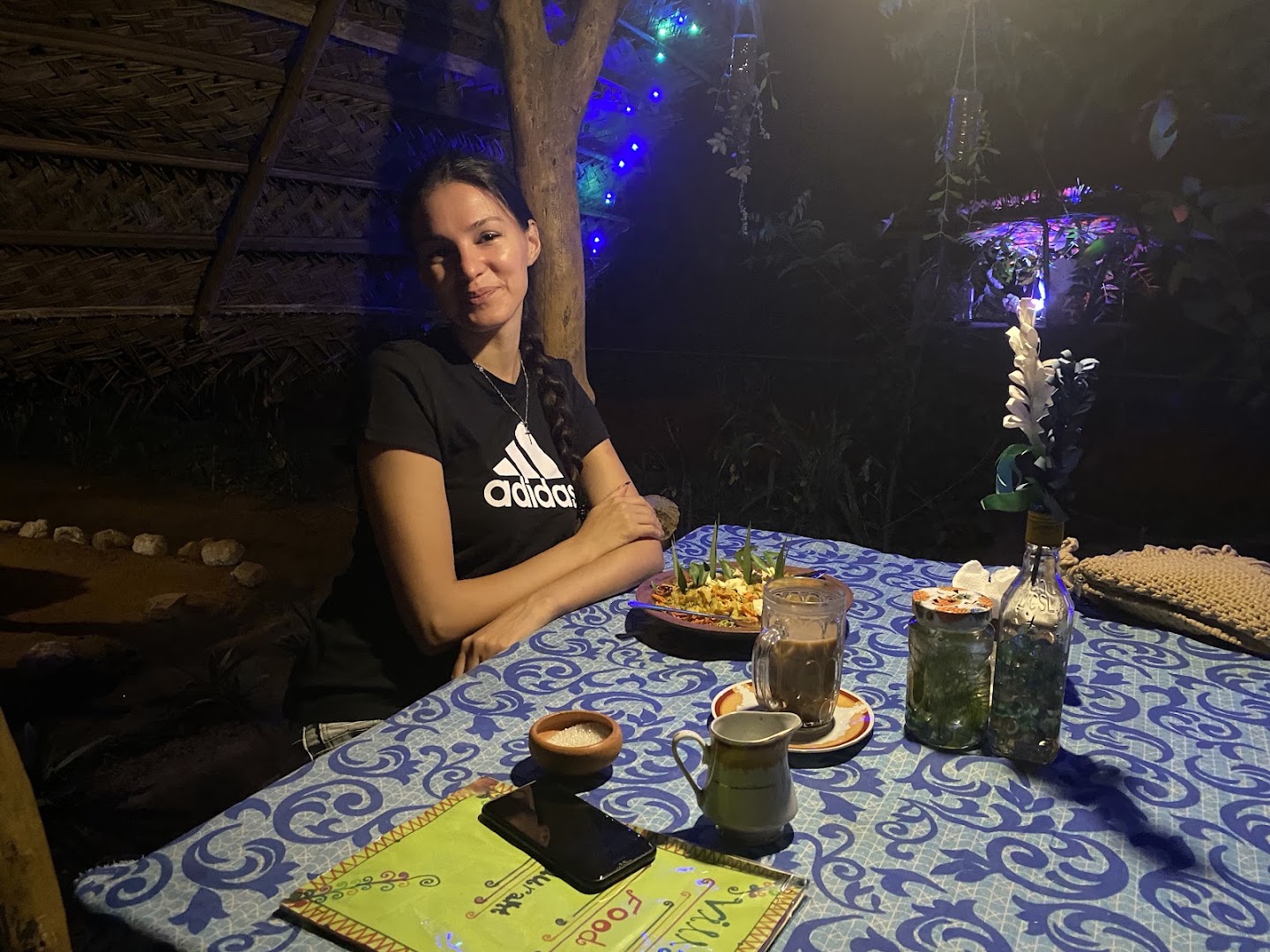 A visitor seated at a garden table with food and drinks in the evening